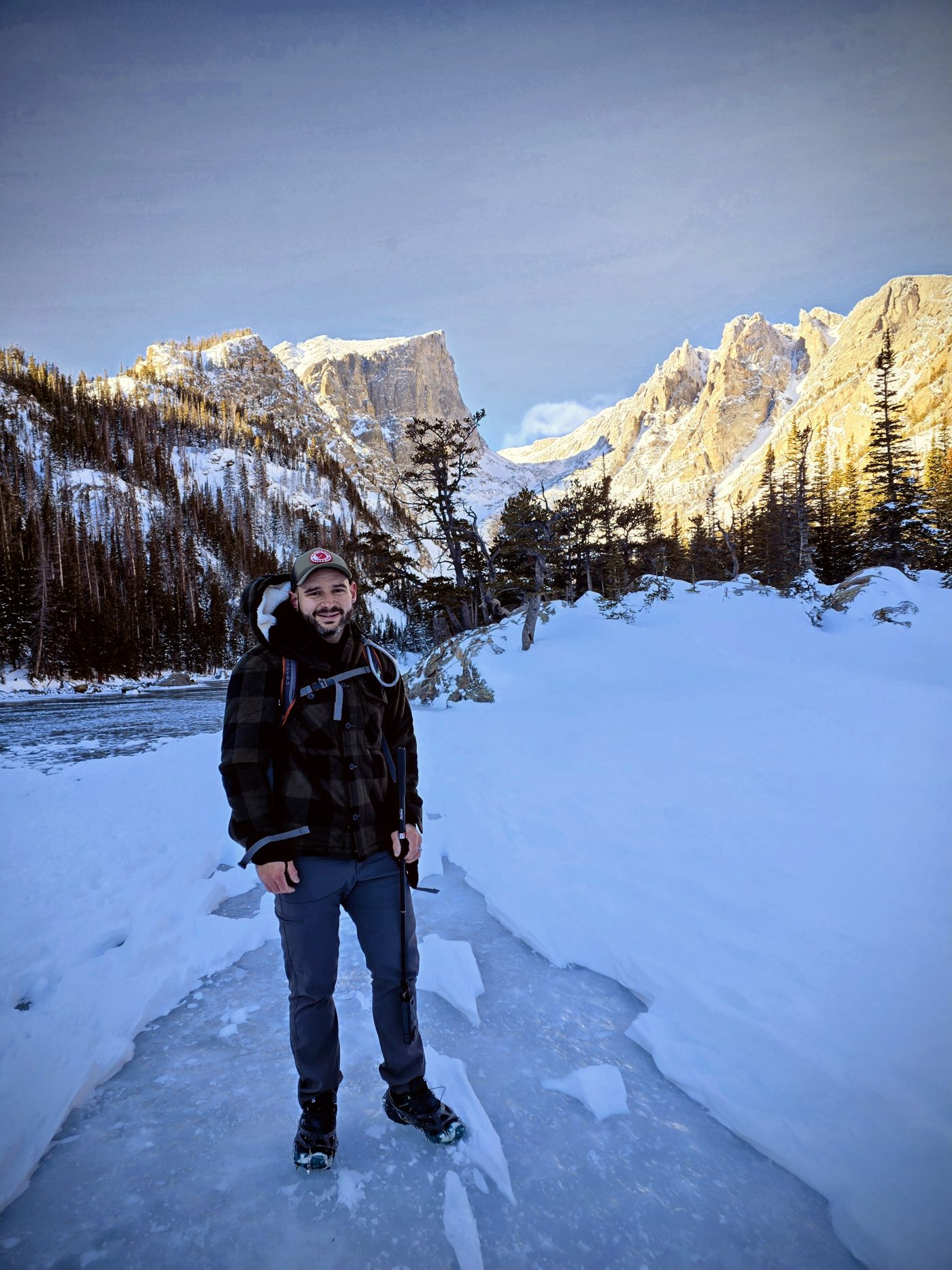 Ty smiling on a frozen trail in Rocky Mountain National Park, snowy peaks behind him